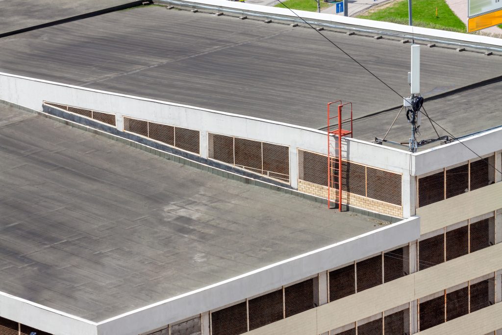 Flat roof top with antenna system and ladder on modern commercial building car garage facade residential area for sale. Urban development concept image